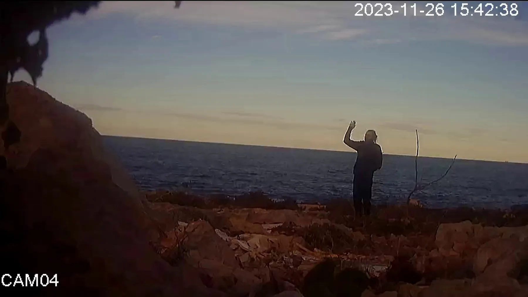 CCTV image of a distant figure raising a hand beside the sea.
