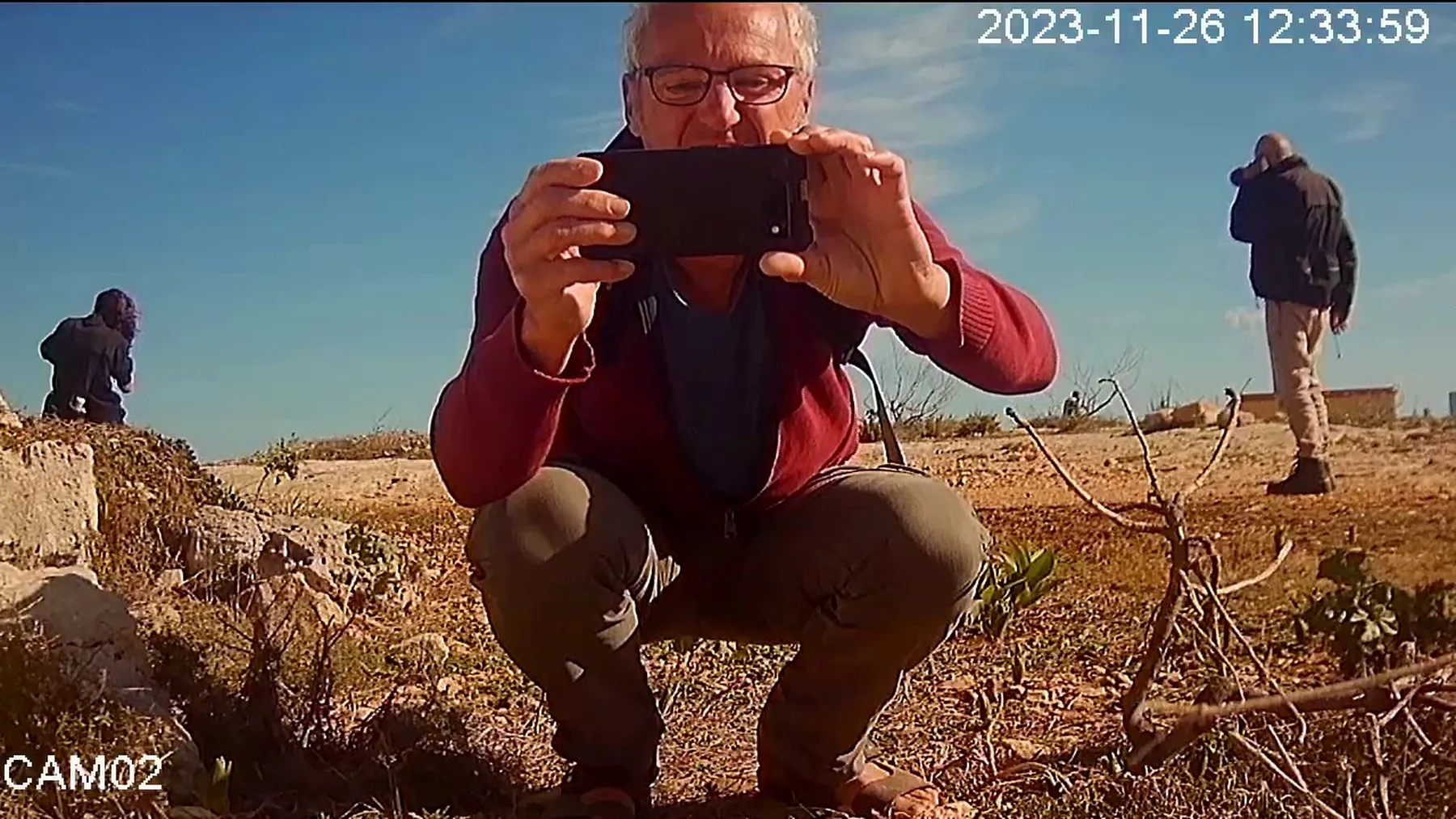 CCTV image of a man photographing with a phone on a rocky hillside.