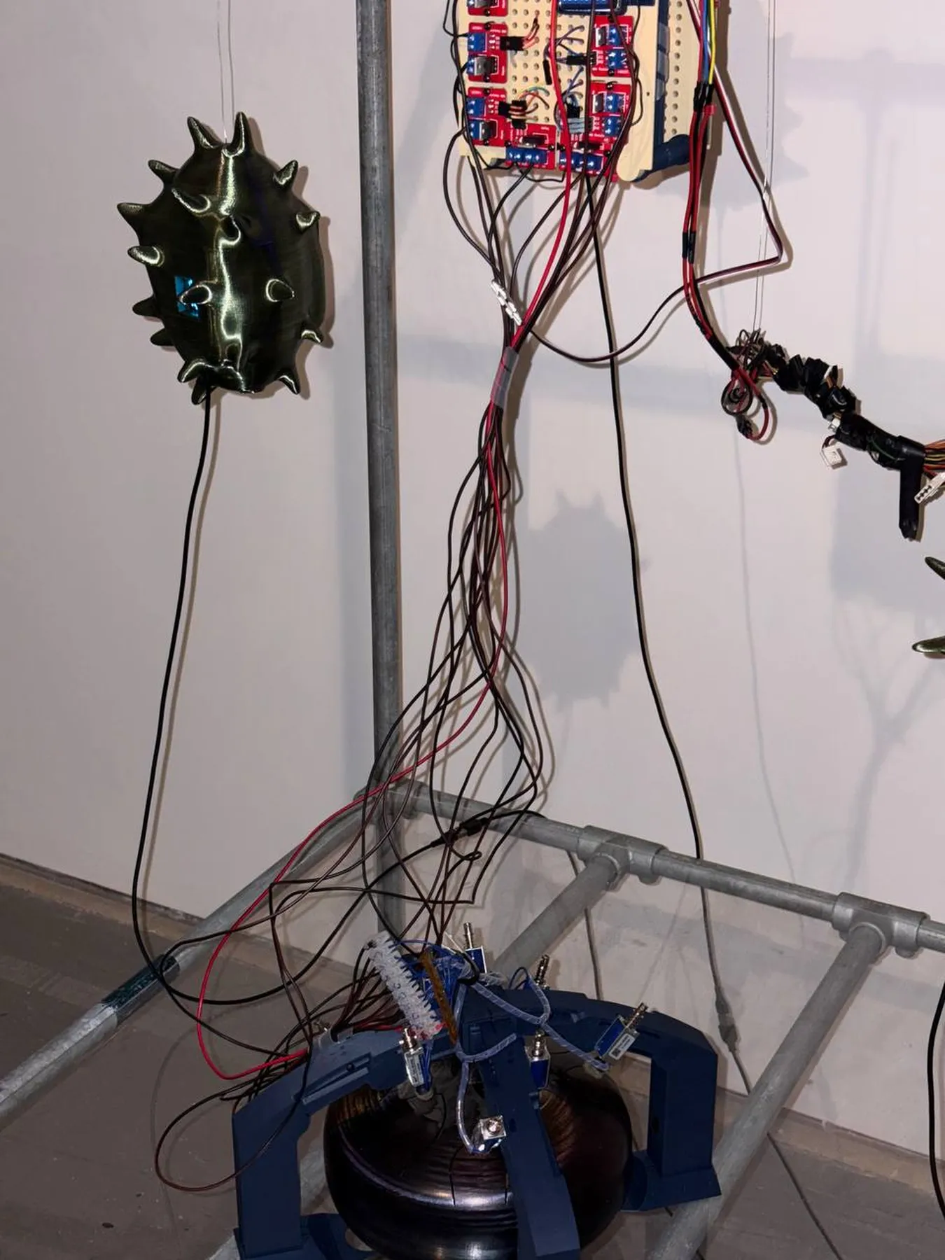 Close view of the C4VE DWELLER installation with a green spiked sculpture, electronics and hanging wires.
