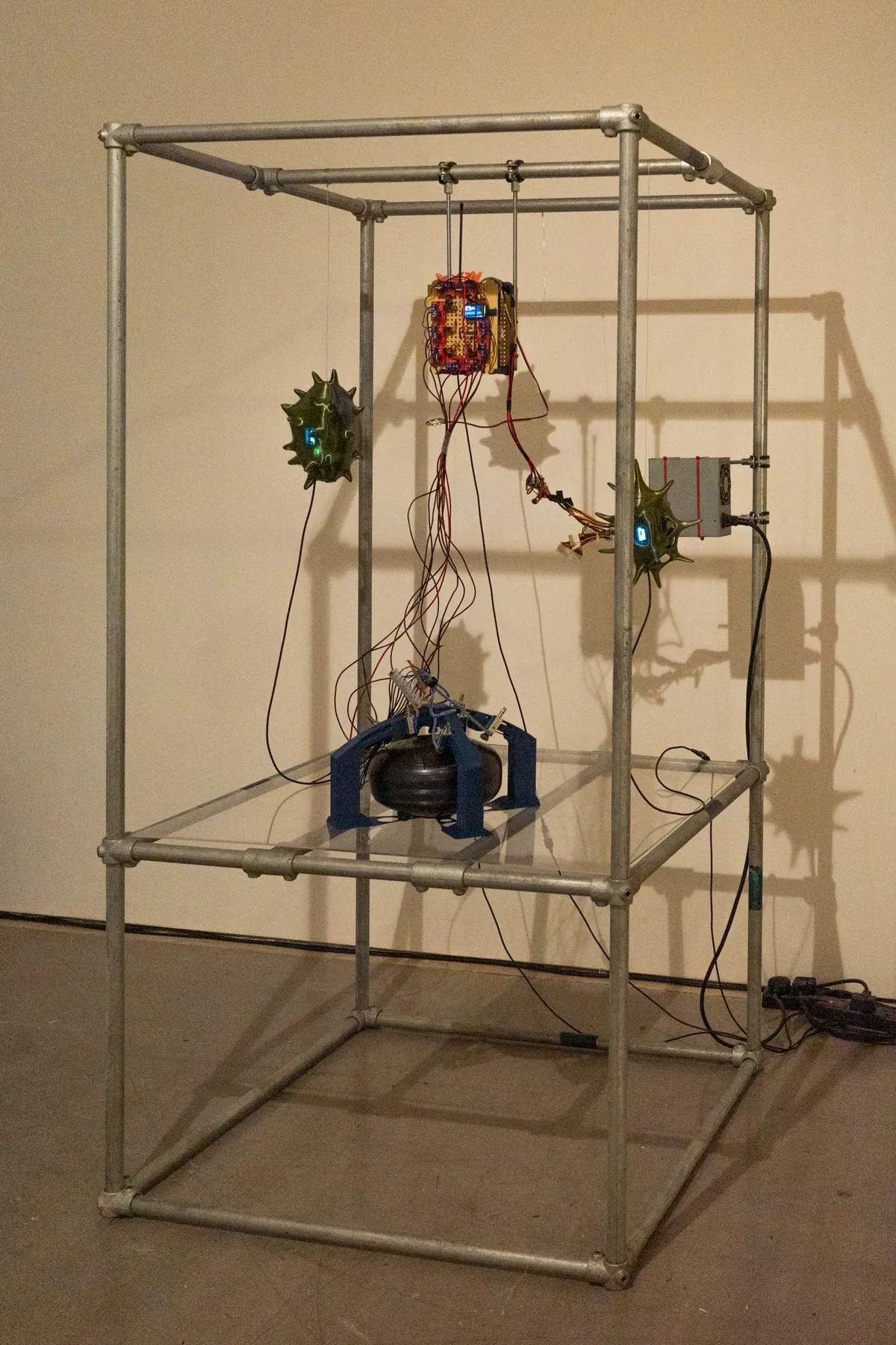 Angled view of the framed installation with suspended sculptures and exposed wiring.